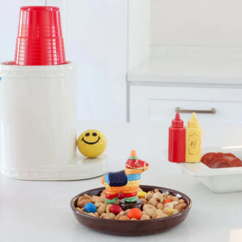 Bowl of dog treats with a toy horse, red cups, and condiment bottles on a white surface.