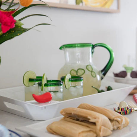 Green pitcher with lime wedges on a white tray with tamales and flowers.