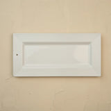 A white rectangular ceramic serving platter with a fluted border, shown against a textured beige wall.
