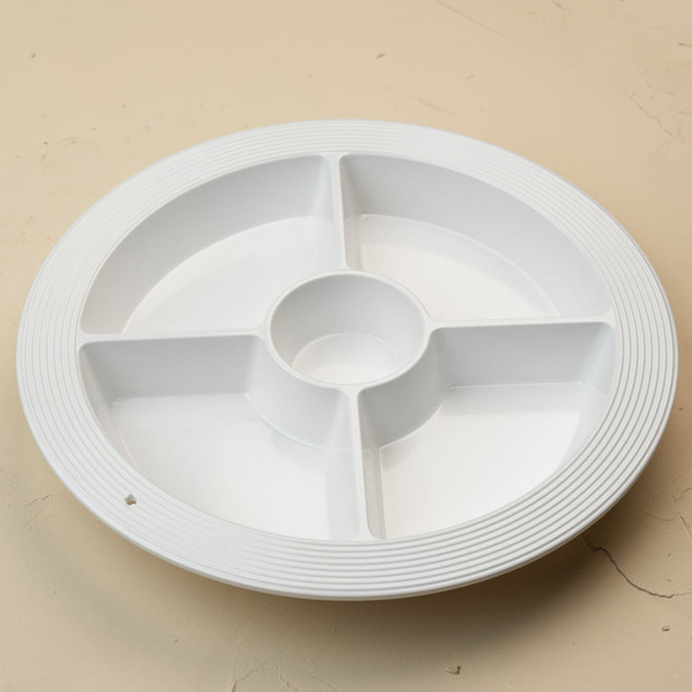 A white circular plastic multi-compartment serving tray with a ribbed outer edge and a central well, shown on a plain beige surface.