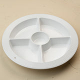 A white circular plastic multi-compartment serving tray with a ribbed outer edge and a central well, shown on a plain beige surface.
