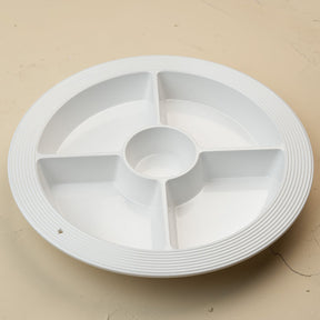 A white circular plastic multi-compartment serving tray with a ribbed outer edge and a central well, shown on a plain beige surface.