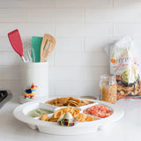 Kitchen counter with a platter of snacks and dips, including tortilla chips and guacamole, with a bag of chips in the background.