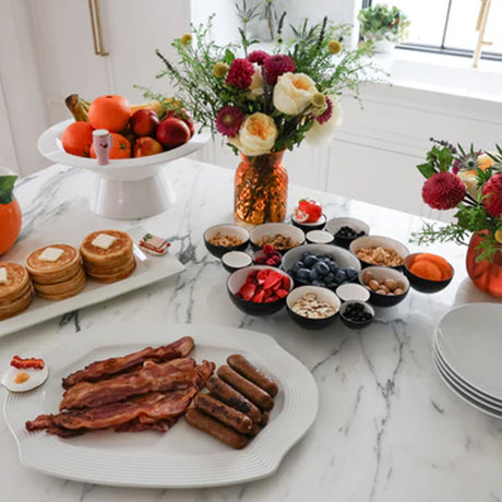 Breakfast spread with pancakes, bacon, and fruit on a marble countertop.
