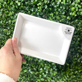 White rectangular tray held by a hand against a green leafy background