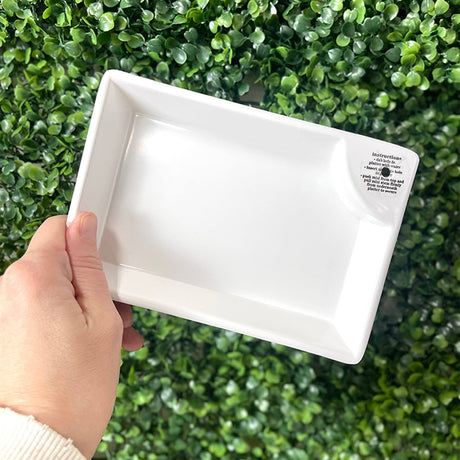 White rectangular tray held by a hand against a green leafy background