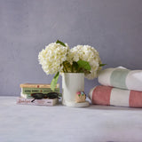 White flowers in a vase on a surface with books and towels in the background.
