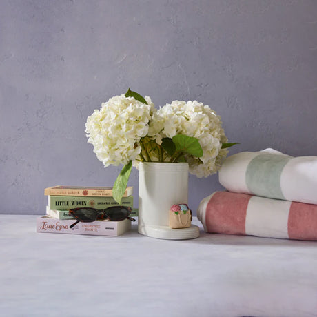 White flowers in a vase on a surface with books and towels in the background.