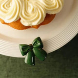 A glossy dark green bow-shaped hair clip or brooch resting on a white plate next to a frosted cupcake.