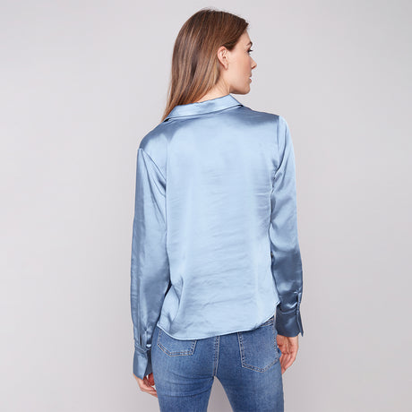 Woman wearing a light blue satin shirt and jeans on a plain background