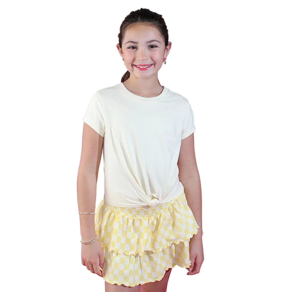 Young girl wearing a white t-shirt and yellow polka dot skirt against a pink background