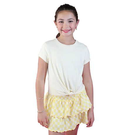 Young girl wearing a white t-shirt and yellow polka dot skirt against a pink background