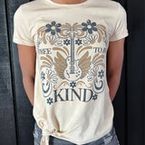 Person wearing a white t-shirt with a guitar graphic and 'Free to be Kind' text.
