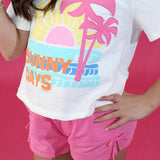 Person wearing a white t-shirt with 'Sunny Days' and palm tree design on a pink background