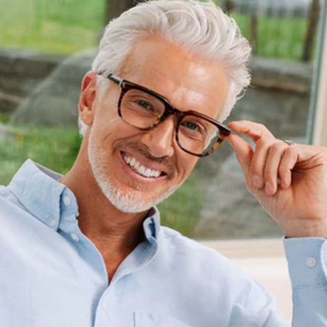 Man adjusting glasses with a blurred outdoor background