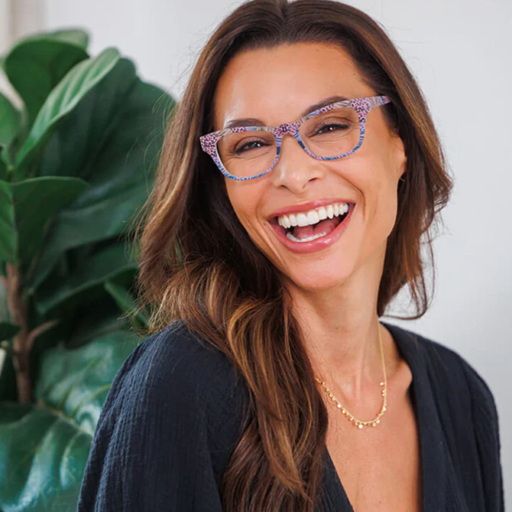 Woman wearing colorful glasses and smiling in front of a plant