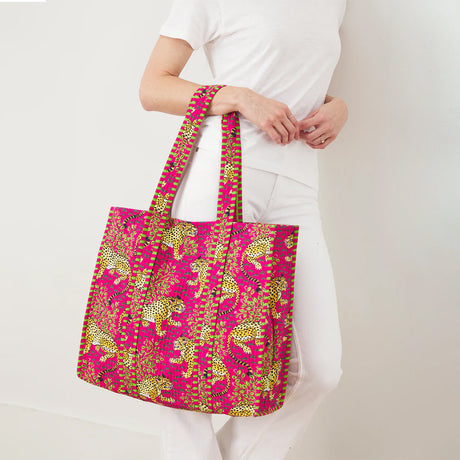 Person holding a pink tote bag with green patterns against a white background