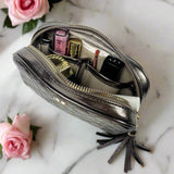 Silver makeup bag with cosmetic items on a marble surface with pink roses.