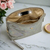 Holographic makeup bag on a marble surface with flowers and a compact mirror.