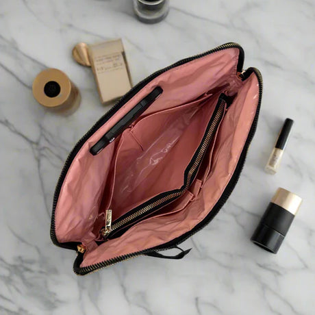 Open makeup bag with pink interior on a marble surface with cosmetic items around