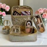 Gold travel makeup case with cosmetic items on a white surface with pink flowers in the background