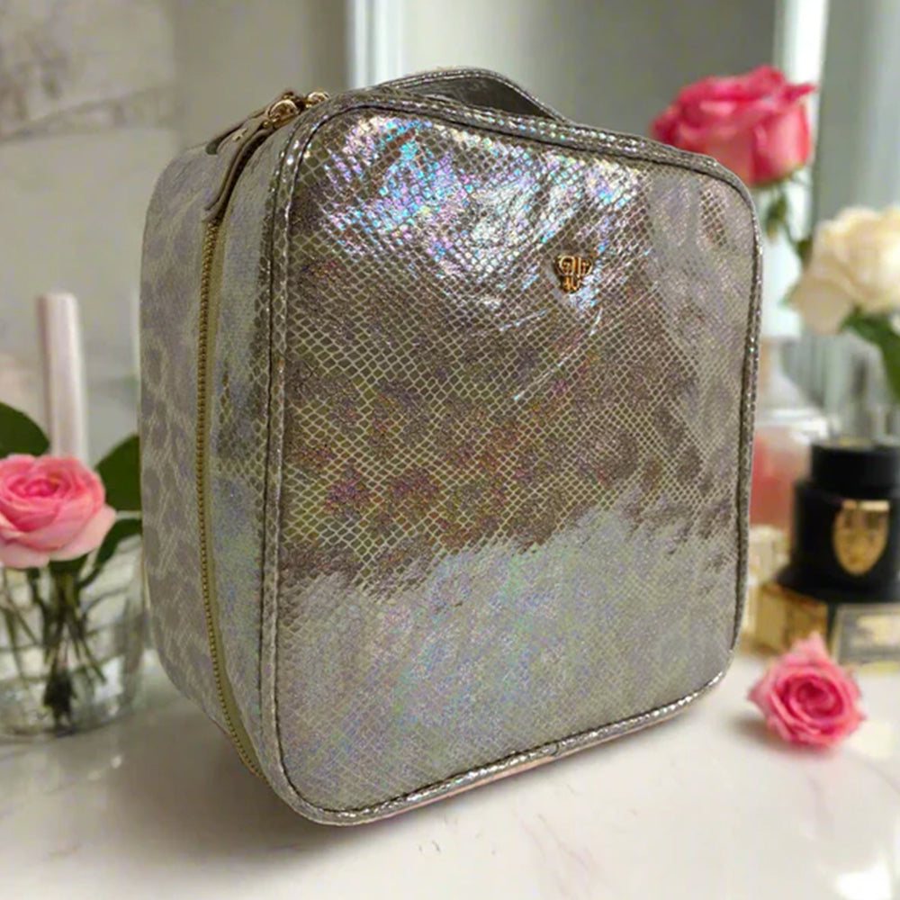 Silver iridescent cosmetic bag on a surface with pink roses and a candle in the background