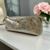 Gold glittery pouch with a gold zipper on a white surface with pink flowers in the background