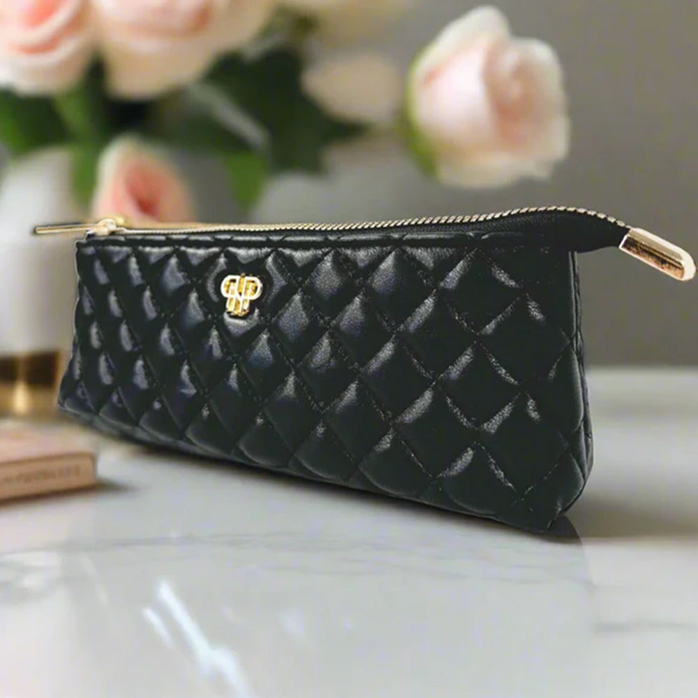 Black quilted wallet with gold clasp on a marble surface with flowers in the background