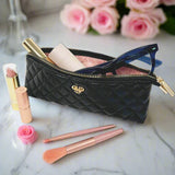 Black quilted makeup bag with cosmetic items on a marble surface with pink roses in the background