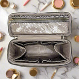 Open makeup bag with marble interior on a marble surface with makeup items around