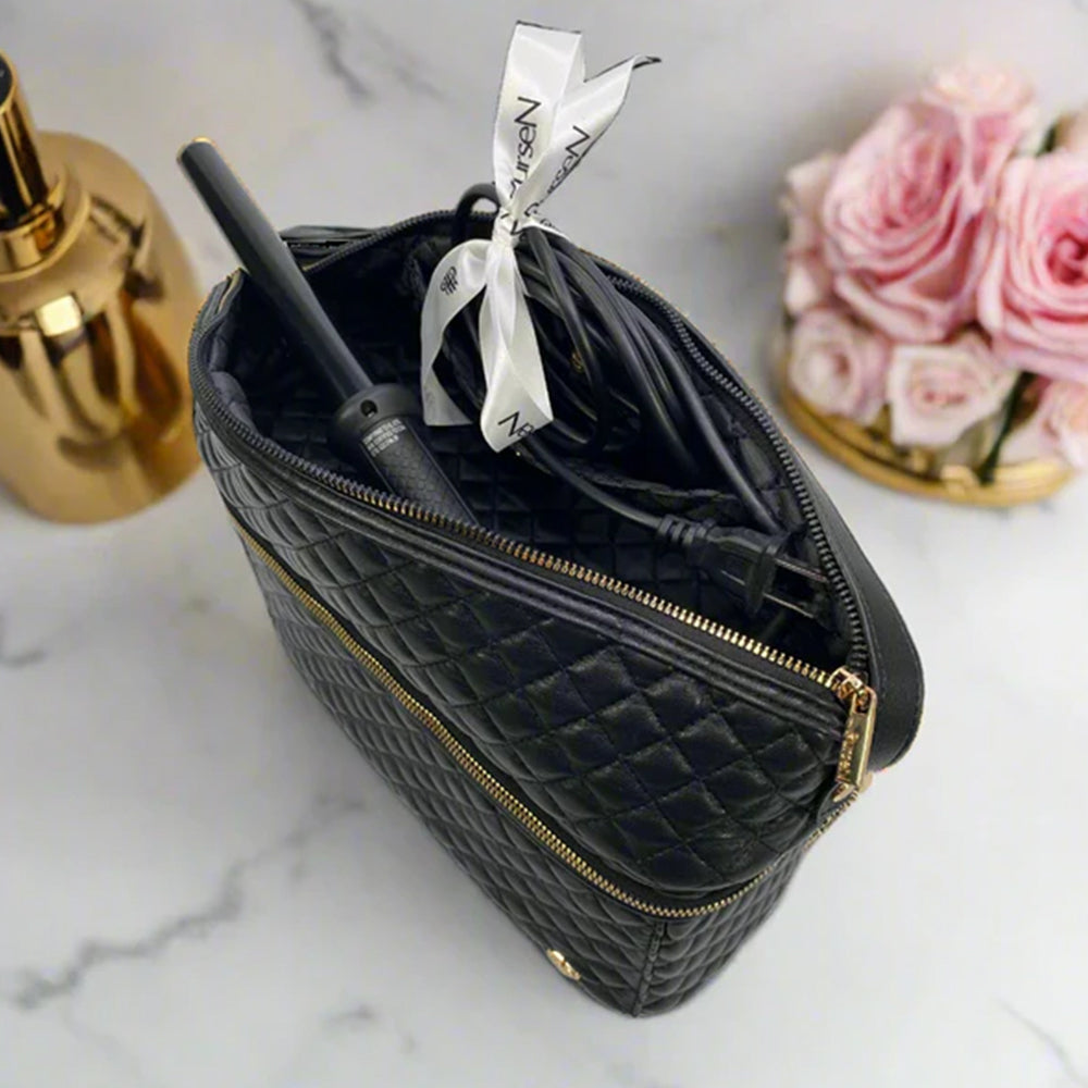 Black quilted makeup bag with gold zipper on a marble surface with roses and a bottle.