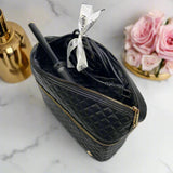 Black quilted makeup bag with gold zipper on a marble surface with roses and a bottle.
