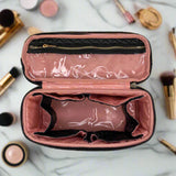 Pink makeup case with black interior on a marble surface with makeup items around