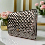 Quilted clutch bag with a brand logo on a white surface with flowers in the background