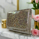 Gold metallic leopard print wallet on a marble surface with flowers and candles in the background