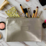 Silver makeup pouch with brushes and other items on a marble surface