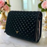 Black quilted handbag on a marble surface with floral decorations in the background