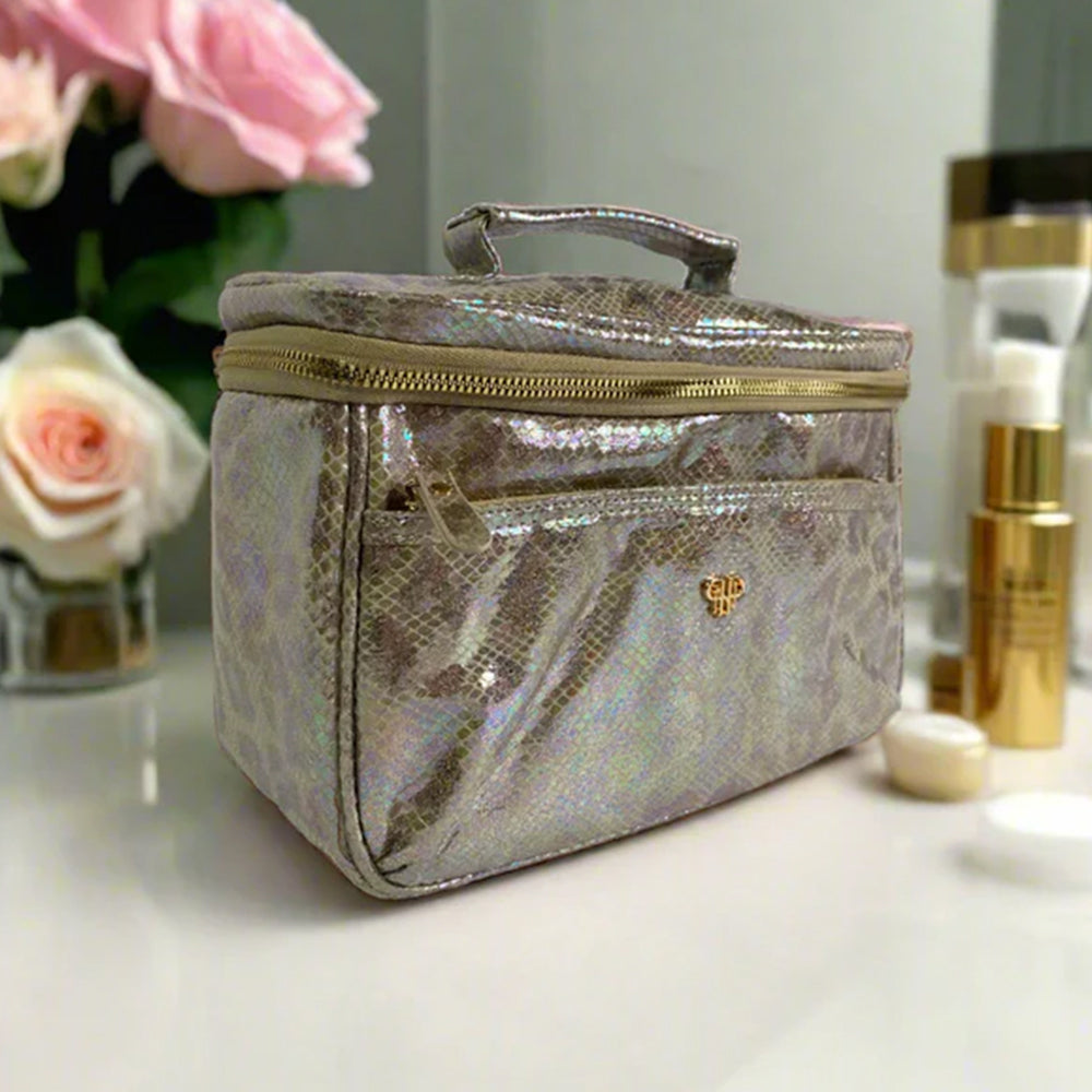 Silver iridescent cosmetic bag on a vanity table with flowers and skincare products.