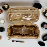 Empty beige makeup case with a clear top compartment on a white background with makeup items.