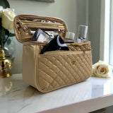 Quilted beige cosmetic bag with makeup items on a reflective surface