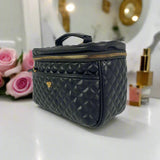 Black quilted cosmetic bag on a vanity with pink roses and perfume bottles.