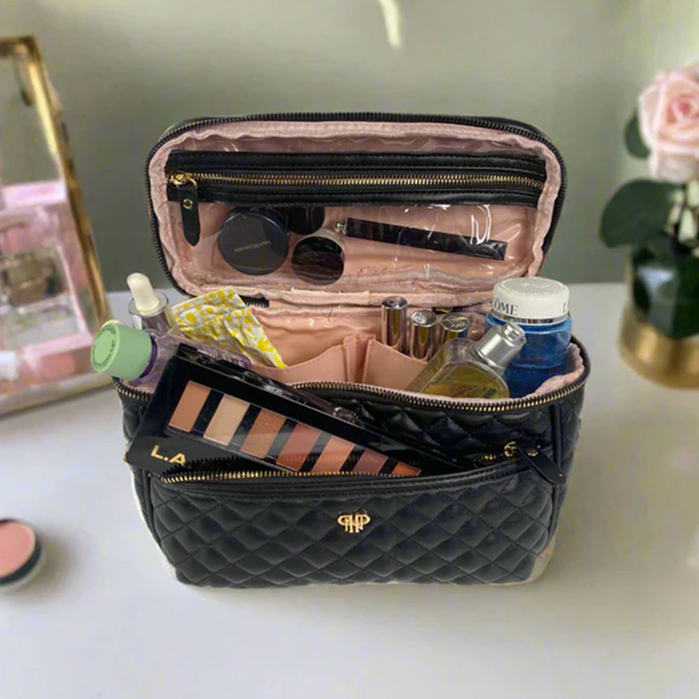 Open black quilted makeup bag with various items on a light surface.