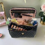 Open black quilted makeup bag with various items on a light surface.