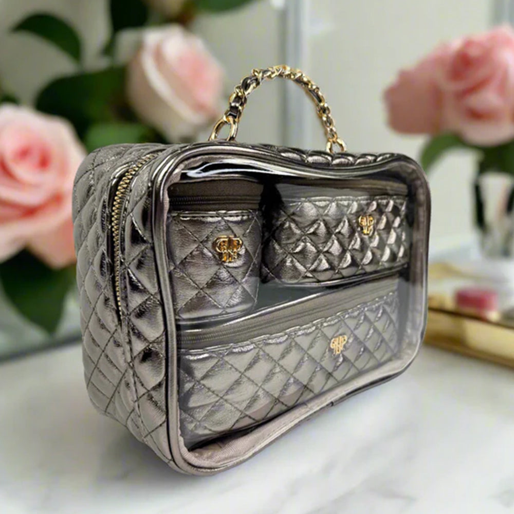 Quilted gray handbag with gold accents on a white surface with pink flowers in the background