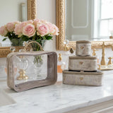 Set of decorative boxes on a marble surface with flowers and mirrors in the background