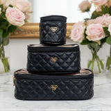 Stack of black quilted cosmetic bags with a logo on a marble surface with flowers in the background