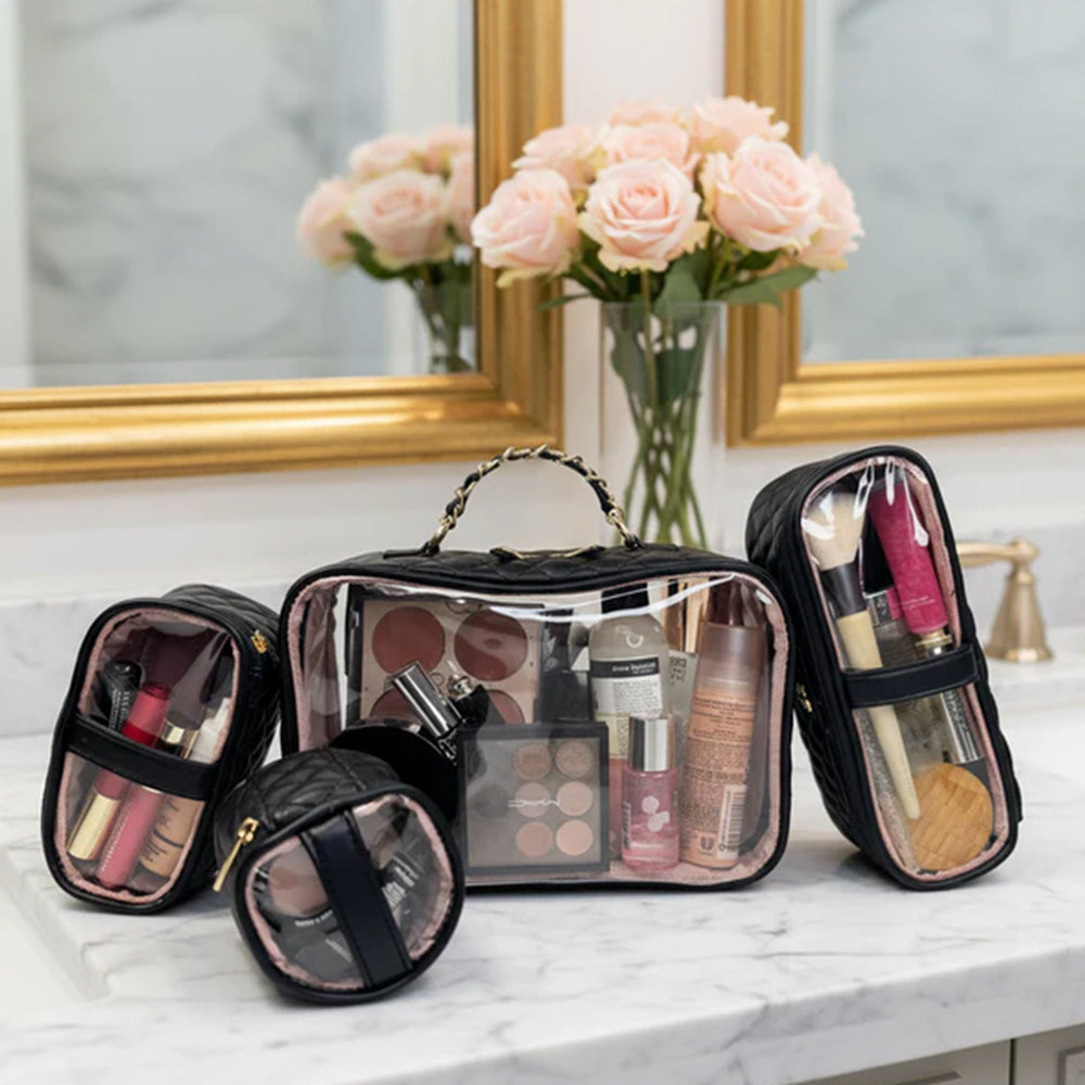 Set of clear makeup bags with cosmetic items on a marble counter with flowers and mirror in the background