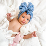 Baby wearing a blue headband with a bow, holding a white plush toy on a white background