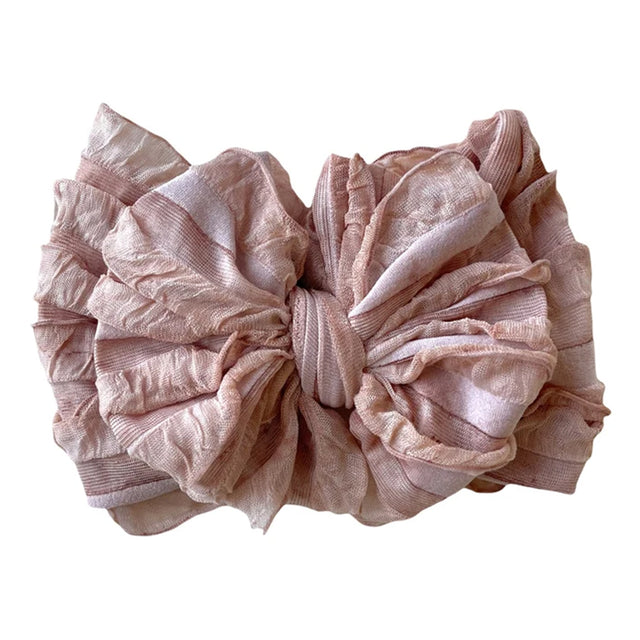 A large, ruffled fabric hair bow in a dusty pink color, photographed flat against a solid white background.