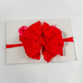 A bright red fabric hair bow with a matching red elastic headband, displayed on a white backing card against a white background.